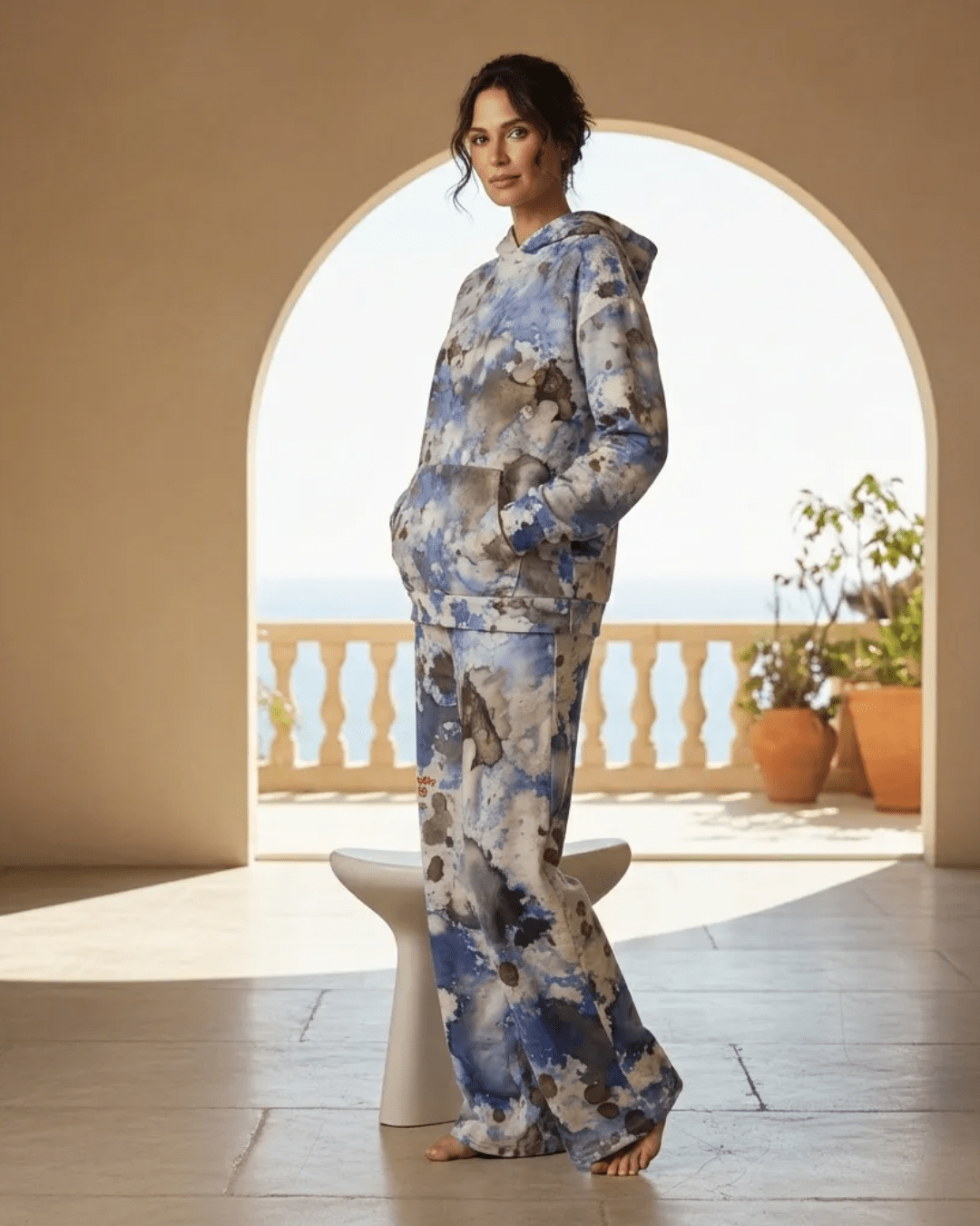 A BunnyBankY AI proprietary model wearing the Amalfi Resort Hoodie and matching wide-leg joggers. The image showcases the fluid light blue, beige, and brown "beach splash" print against a minimalist background, highlighting the relaxed, high-fashion silhouette.