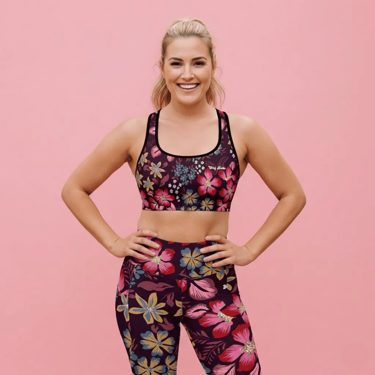 A BunnyBankY AI proprietary model wearing the Green Park Performance Bra and matching sculpt leggings in blue, pink, yellow floral pattern on burgundy background