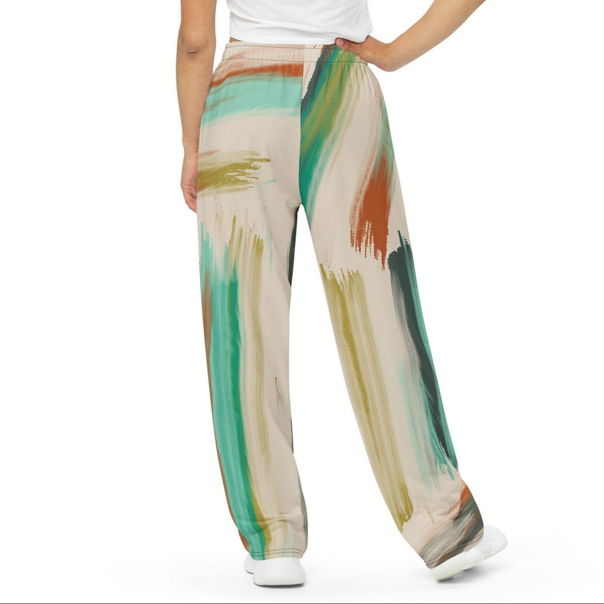 A woman modeling the artful aura flow joggers. high-waisted, wide-leg pants featuring an abstract brushstroke pattern in beige, brown, teal, and green, set against a plain white background.