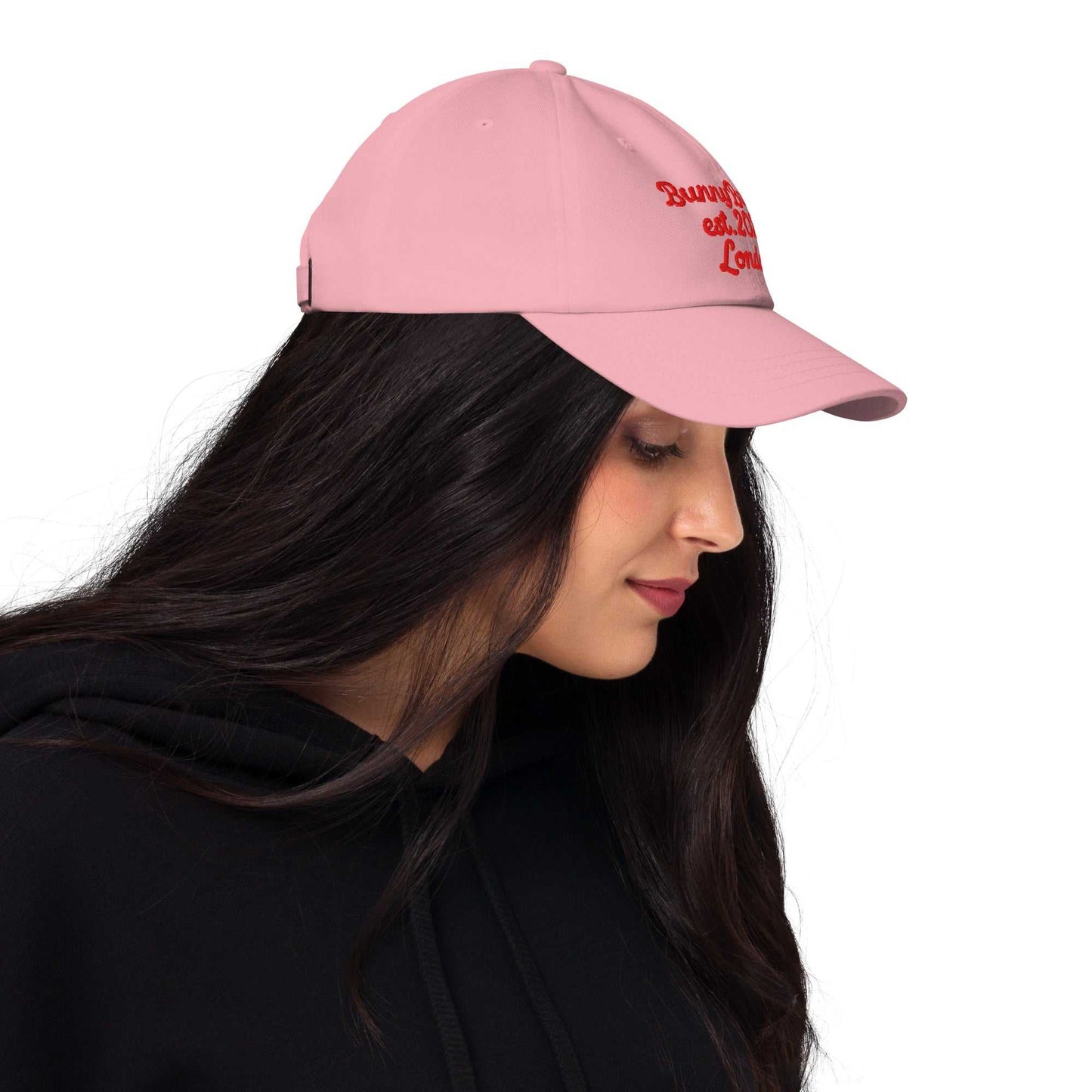 A model wearing The Heritage Cap in pink showing the heriatage branded signature embroidered in red