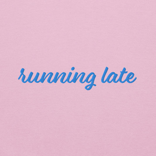 A close-up of The Running Late Sweatshirt, highlighting the "Running Late" embroidery and the iconic heart logo on the sleeve.