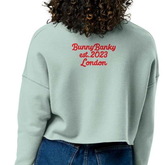 A model wearing The Sisterhood Crop Sweatshirt, showing the raw hem, dropped shoulder cut, and the embroidered "Female Culture" motto on the chest and heritage signature printed at the back