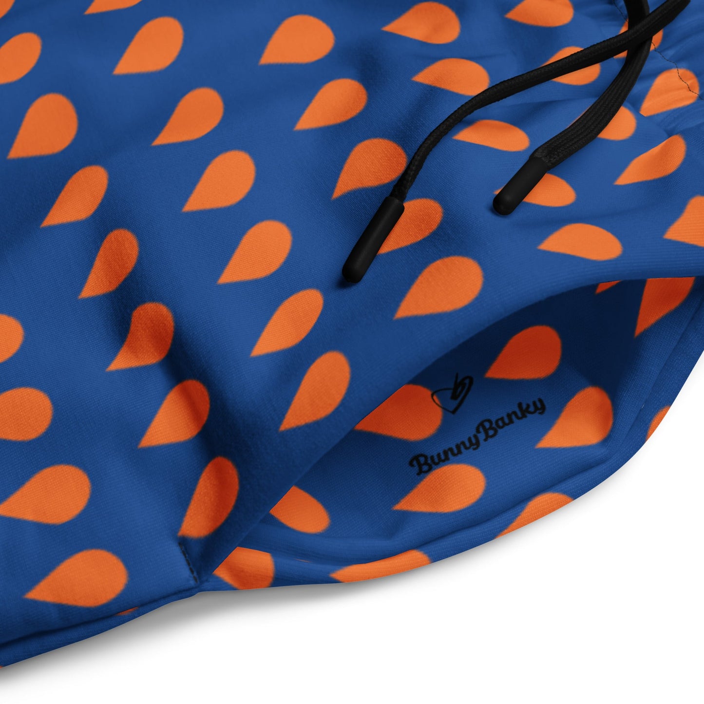 A close up of The Thames Flow Joggers, showing the wide-leg, relaxed silhouette and the orange drop print on the deep navy blue background and the iconic signature inside the pocket in black.