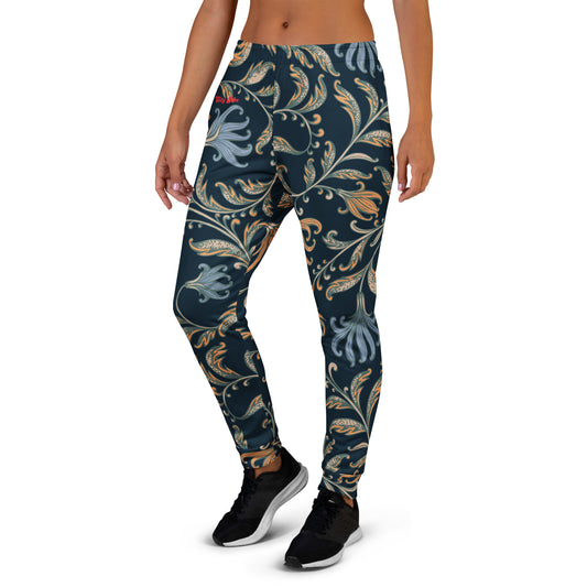 A model wearing the Venice slim fit high-waisted athletic joggers with a dark navy blue background and an intricate botanical pattern in gold, beige, and light blue. The joggers feature a small red logo on the left hip.