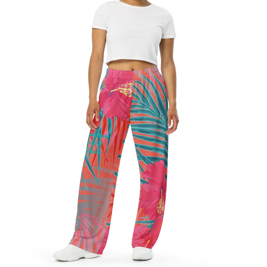 A  model wearing the District Tropics Wide-Leg Joggers and white t-shirt. The image highlights the flowing silhouette and the vibrant pink, orange, and blue tropical floral pattern.