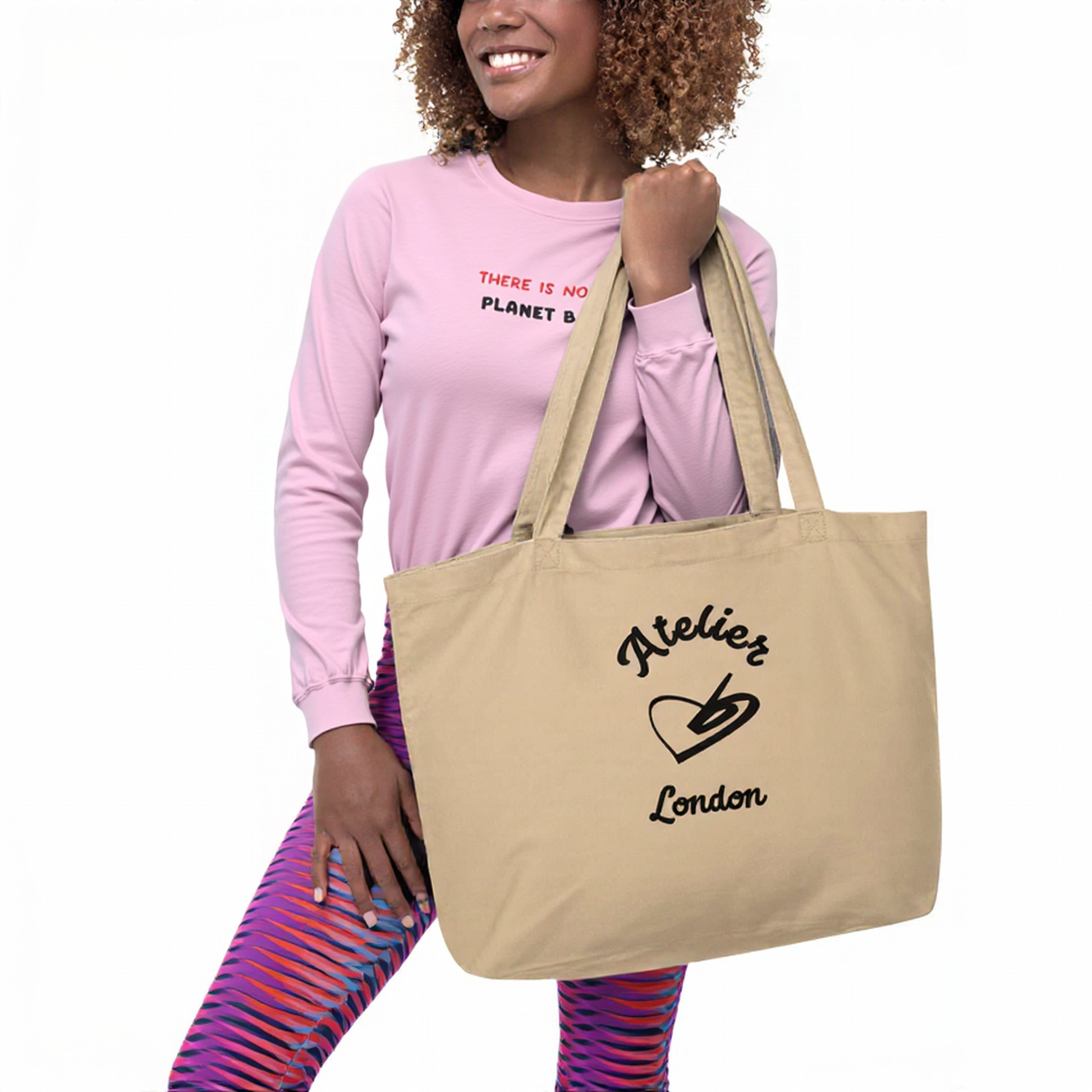 A model holding The Never Full Atelier Tote (featuring the Atelier Heart emblem) while wearing The Moorgate Sculpt Leggings (in the dynamic graphic arrow print) and The Manifesto Sweatshirt (with the 'No Planet B' embroidery).