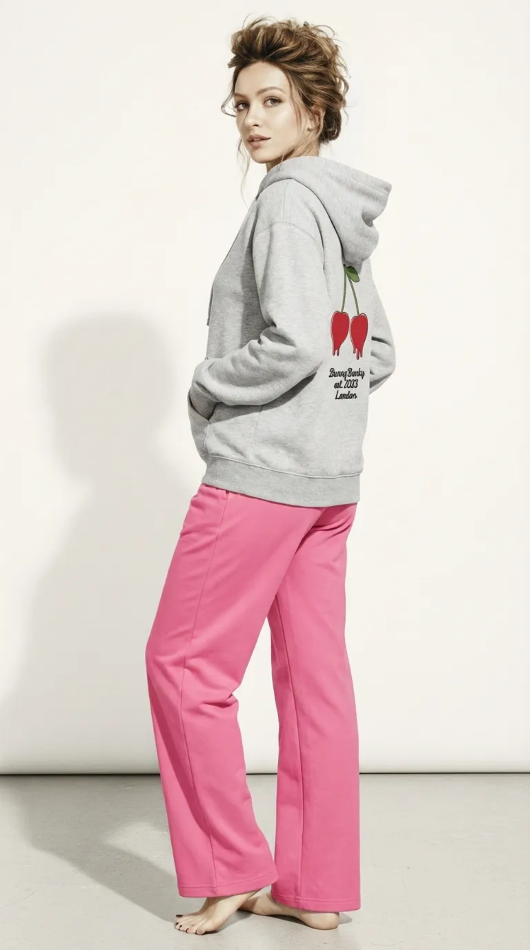 A BunnyBnakY AI proprietary model wearing The Angel Wellness Hoodie, featuring the playful, pop-art cherry print and the heritage signature on the sleeve.