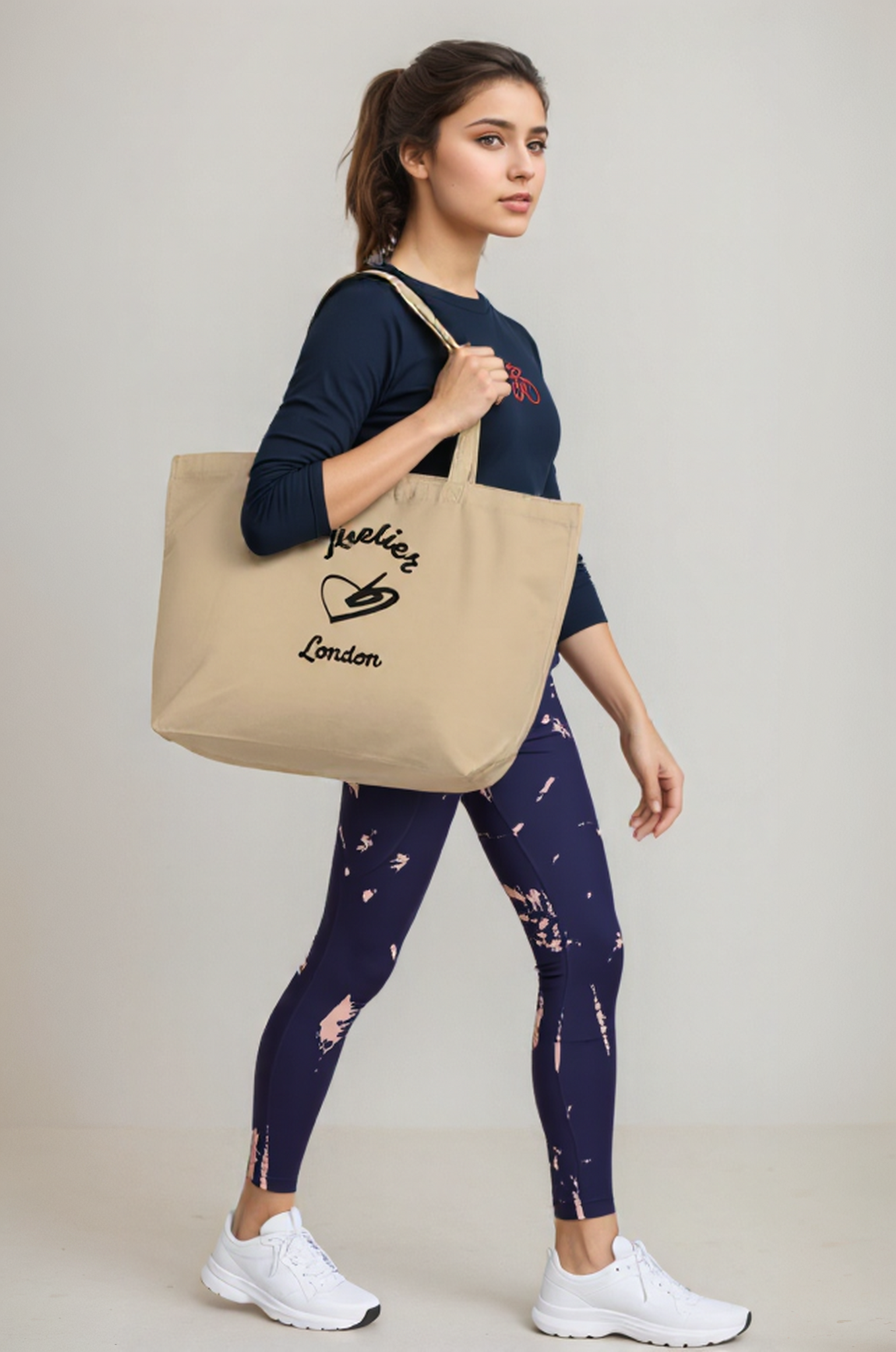 A model holding The Never Full Atelier Tote (featuring the Atelier Heart emblem) while wearing The Bristol Sculpt Leggings (in the dynamic graphity print) and The  Sweatshirt (with the red bicycle embroidery).