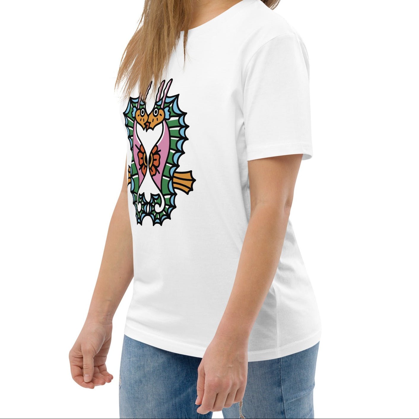 A model wearing the white organic t-shirt featuring a symmetrical graphic of two colorful seahorses with bunny ears and floral details.