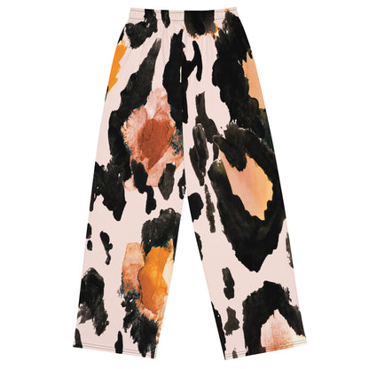 The Amazonia Flow Joggers, a pair of wide-leg pants featuring an abstract watercolor-style print with black, orange, and peach paint strokes on a light pink base, shown against a plain white background.
