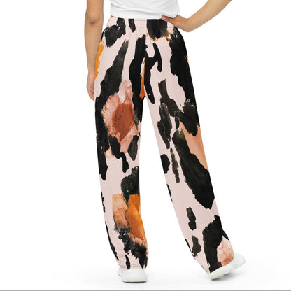 The Amazonia Flow Joggers, a pair of wide-leg pants featuring an abstract watercolor-style print with black, orange, and peach paint strokes on a light pink base, shown against a plain white background.