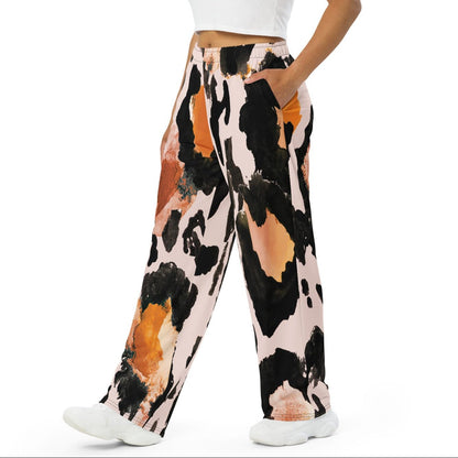 The Amazonia Flow Joggers, a pair of wide-leg pants featuring an abstract watercolor-style print with black, orange, and peach paint strokes on a light pink base, shown against a plain white background.
