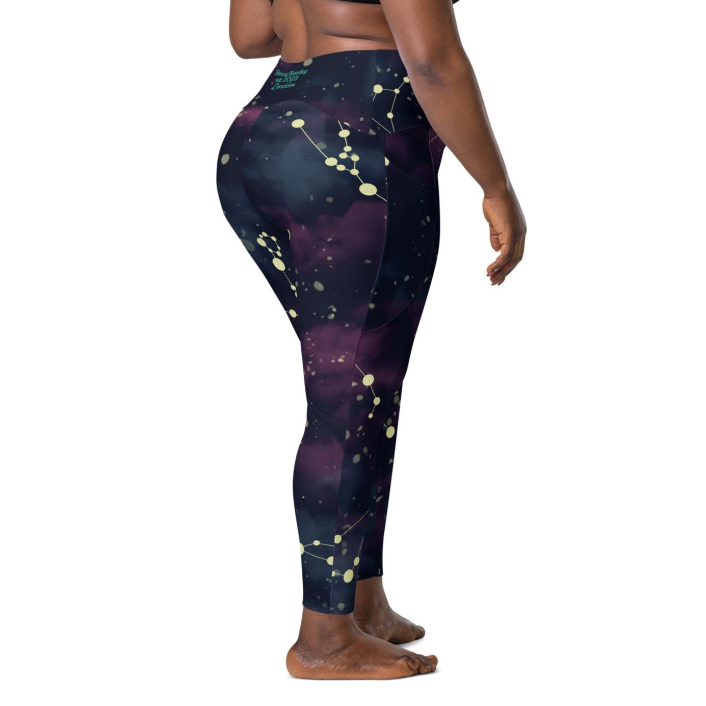 A model wearing The Andromeda Sculpt Leggings, showcasing the sculpting fit and the distinctive yellow star constellation print on the dark purple-to-black gradient fabric. The background features a subtle cosmic nebula.