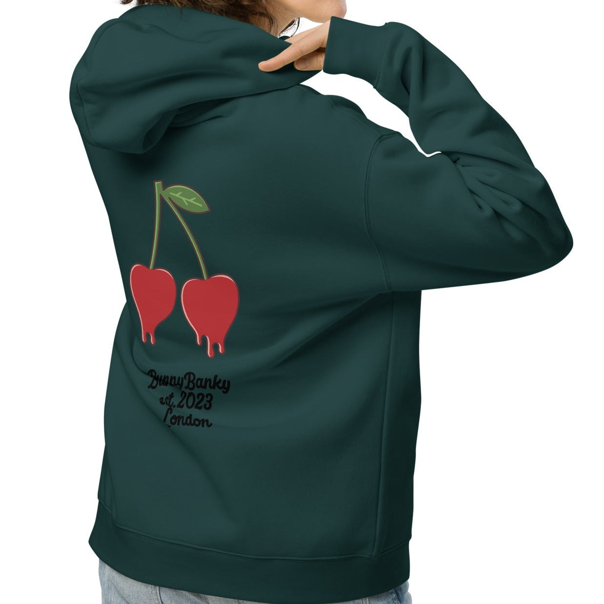 A model wearing The Angel Wellness Hoodie, featuring the playful, pop-art cherry print and the heritage signature on the sleeve.