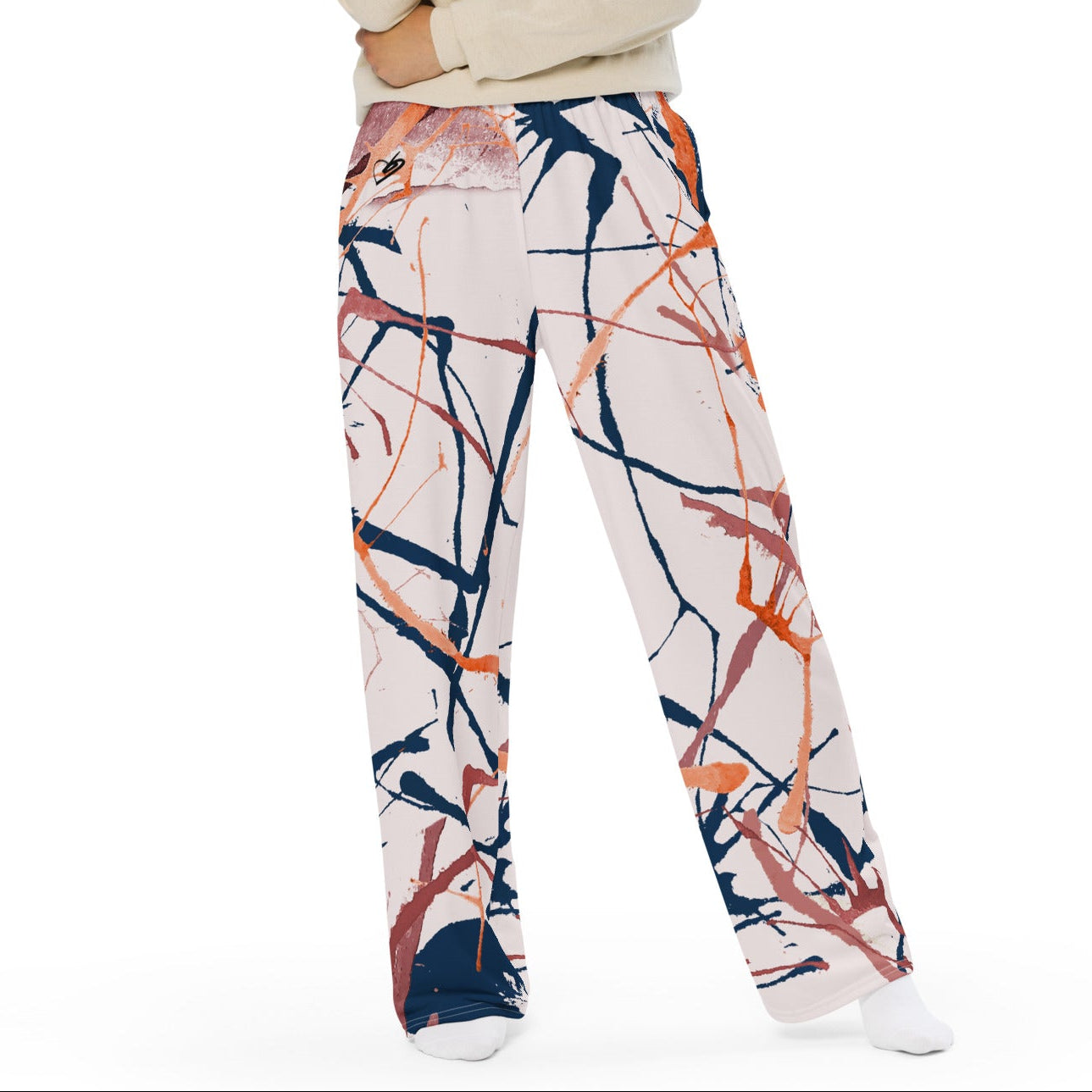 A woman modeling the angle flow wide-leg pants with an abstract paint stroke pattern in navy, orange, and pink on a cream background, paired with a cream long-sleeve top, against a solid white background.