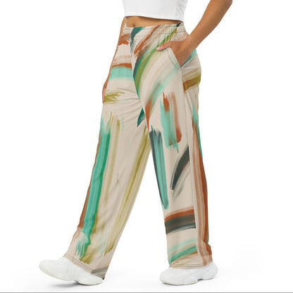 A woman modeling the artful aura flow joggers. high-waisted, wide-leg pants featuring an abstract brushstroke pattern in beige, brown, teal, and green, set against a plain white background.