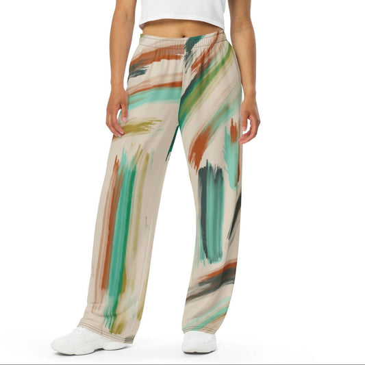 A woman modeling the artful aura flow joggers. high-waisted, wide-leg pants featuring an abstract brushstroke pattern in beige, brown, teal, and green, set against a plain white background.