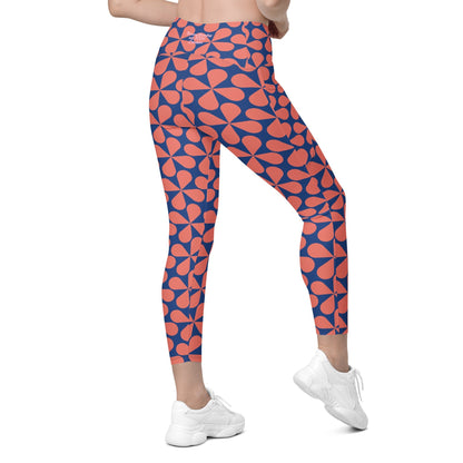 Model wearing the  Bakerloo Sculpt Leggings in geometric pattern in blue with coral background.