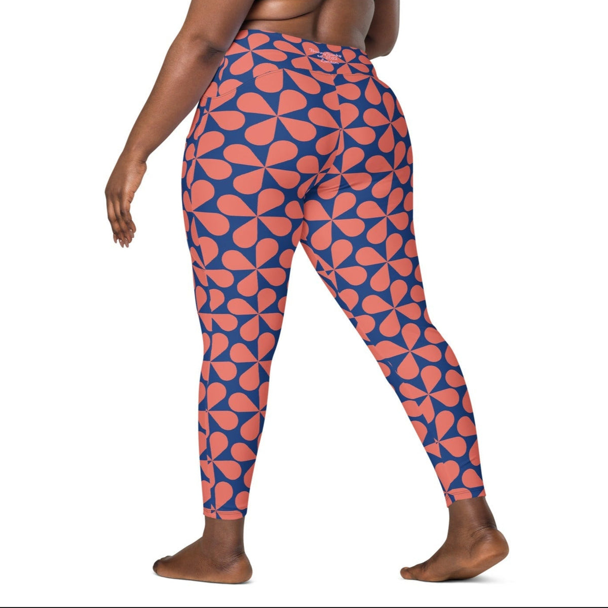 Model wearing the  Bakerloo Sculpt Leggings in geometric pattern in blue with coral background.