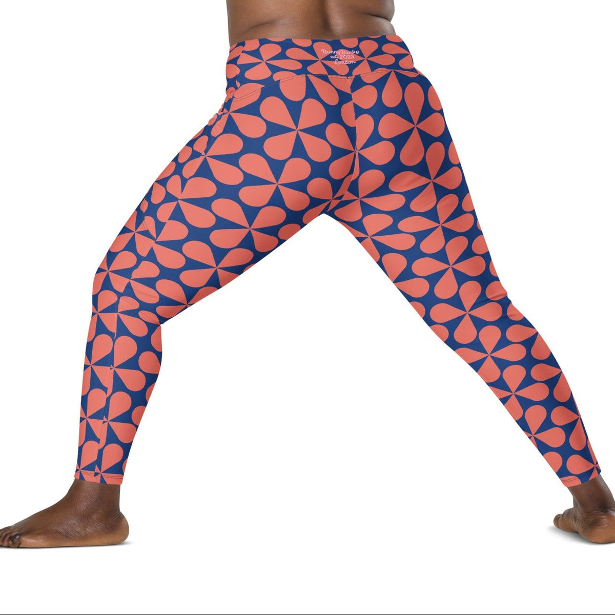 Model wearing the  Bakerloo Sculpt Leggings in geometric pattern in blue with coral background.