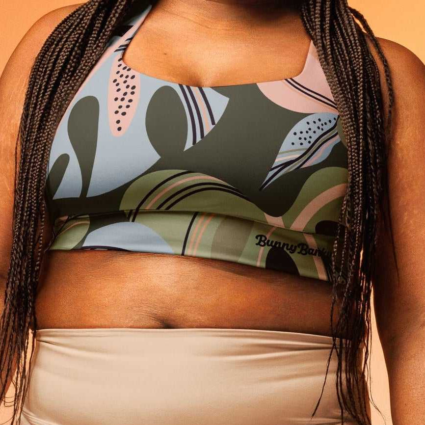 A model wearing The Barbican Longline Performance Bra, showing the supportive longline cut and the pastel green and pink exotic flower print.