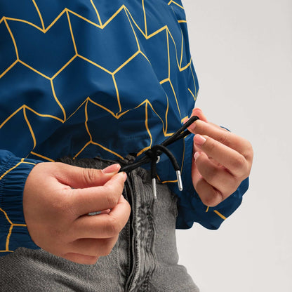 A close-up of The Baron's Court Windbreaker's navy blue and yellow Art Deco print, showing the recycled technical fabric, zip, and quality stitching.