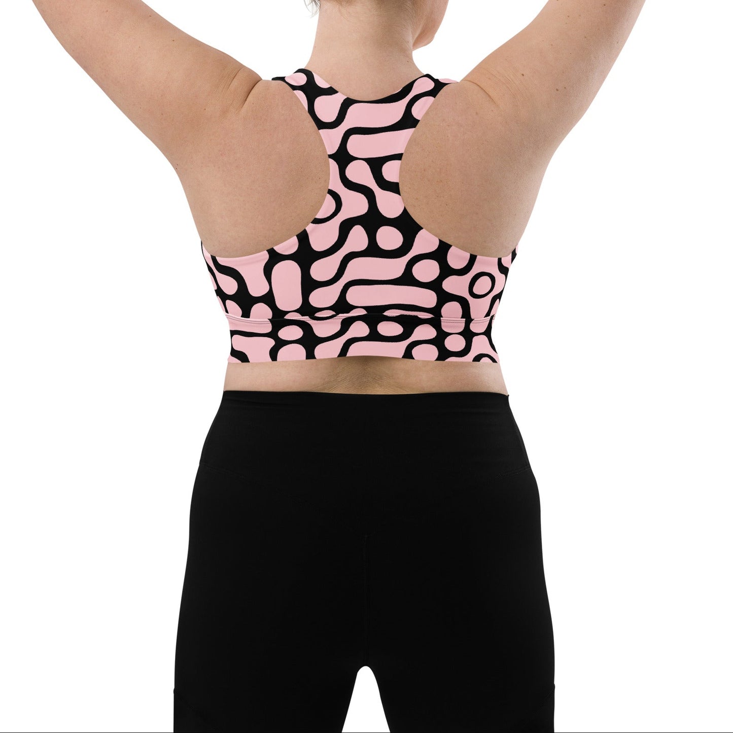 A model wearing the Berlin Performance Bra in black geometric floral pattern on pink background