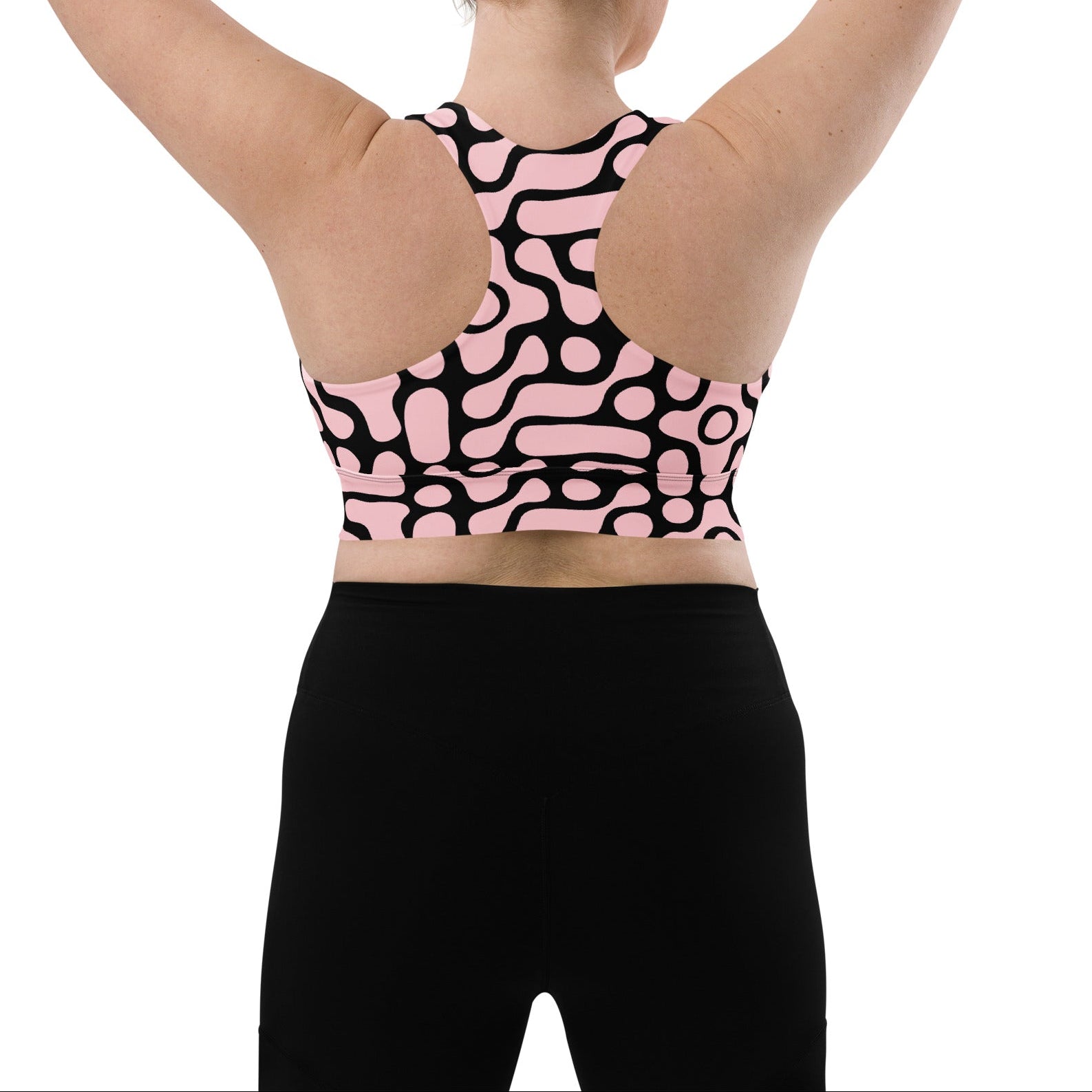 A model wearing the Berlin Performance Bra in black geometric floral pattern on pink background