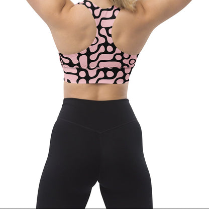 A model wearing the Berlin Performance Bra in black geometric floral pattern on pink background