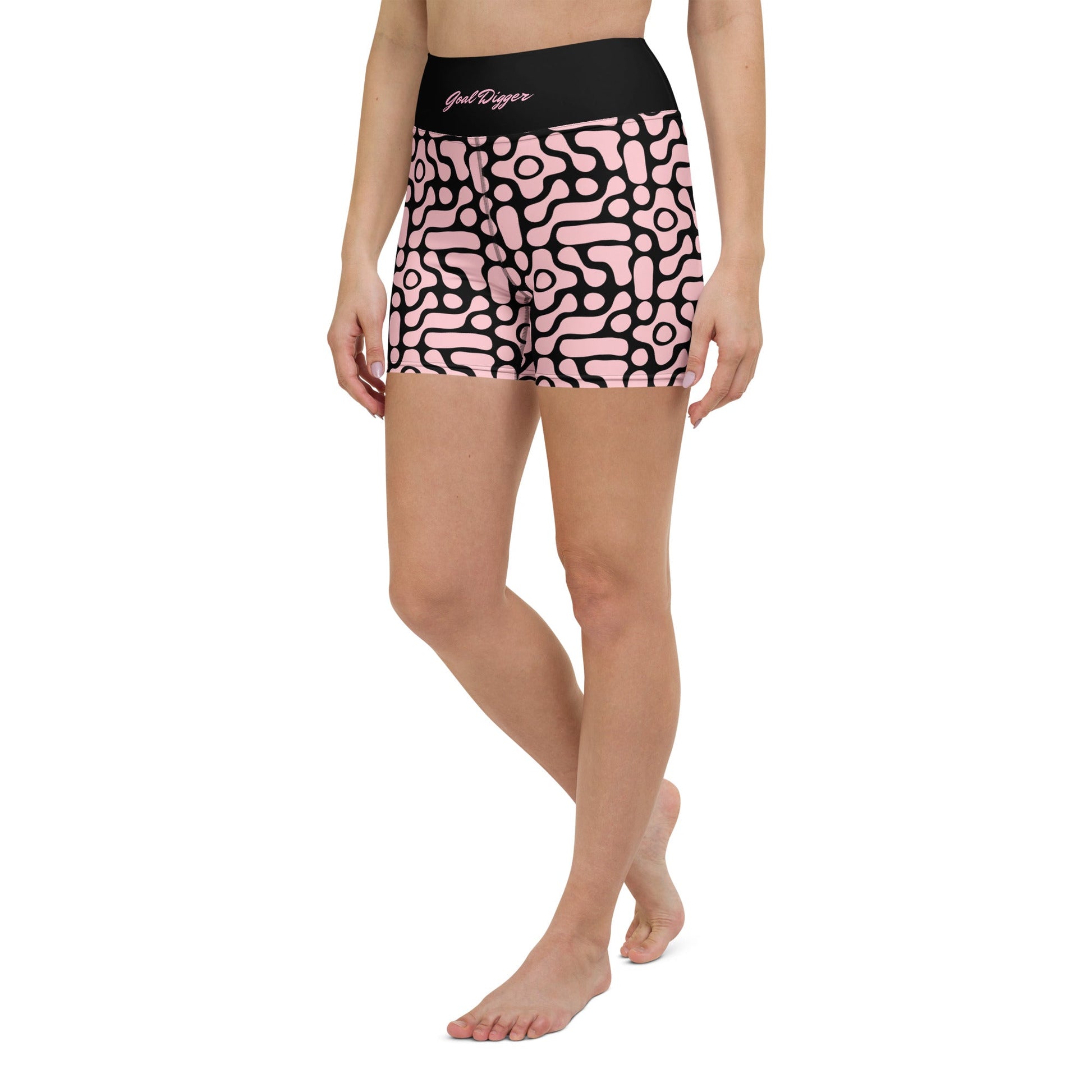 A close-up front view of BunnyBanky performance shorts featuring a bold, custom-designed geometric black floral pattern on a soft pink base. The high-waisted black compression waistband prominently displays the text "GOAL DIGGER" in a stylised, matching pink font. The shorts are designed for a snug, performance fit, shown here as part of a coordinated athletic set against a solid pink studio background.