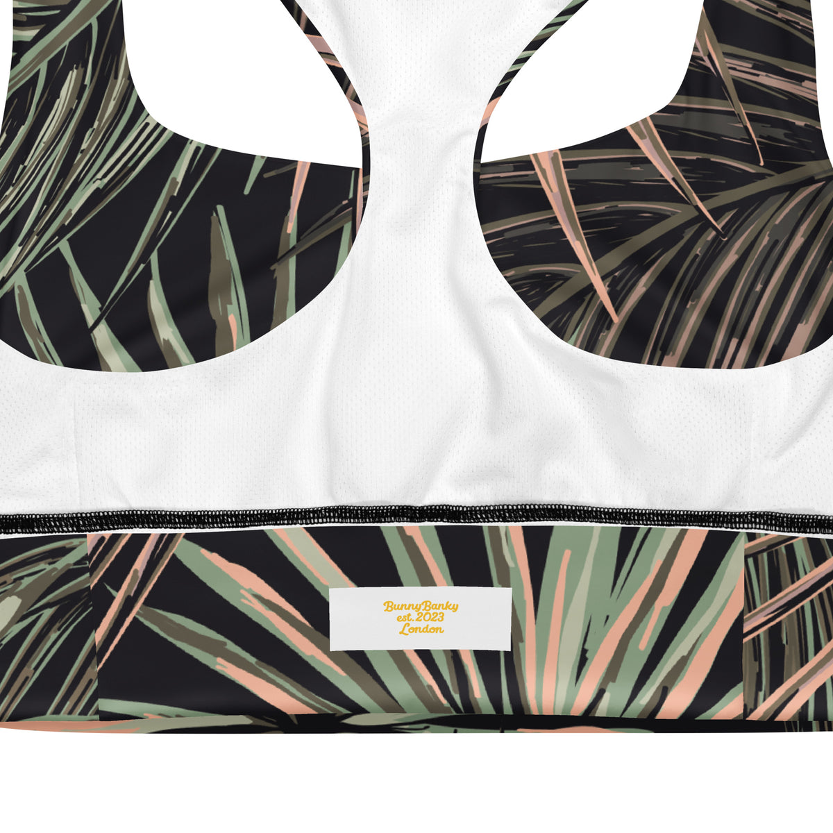 Close-up of the inside back of the chiswick longline performance bra.a sports bra showing a white mesh fabric, underwire cups with a black tropical palm leaf print, and a matching printed underband with a visible bunnybanky  interior label.