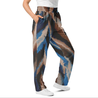 Model wearing the wide-leg Côte d'Azur Flow Joggers in blue and beige earth-tone brushstroke print with hands in side pockets.