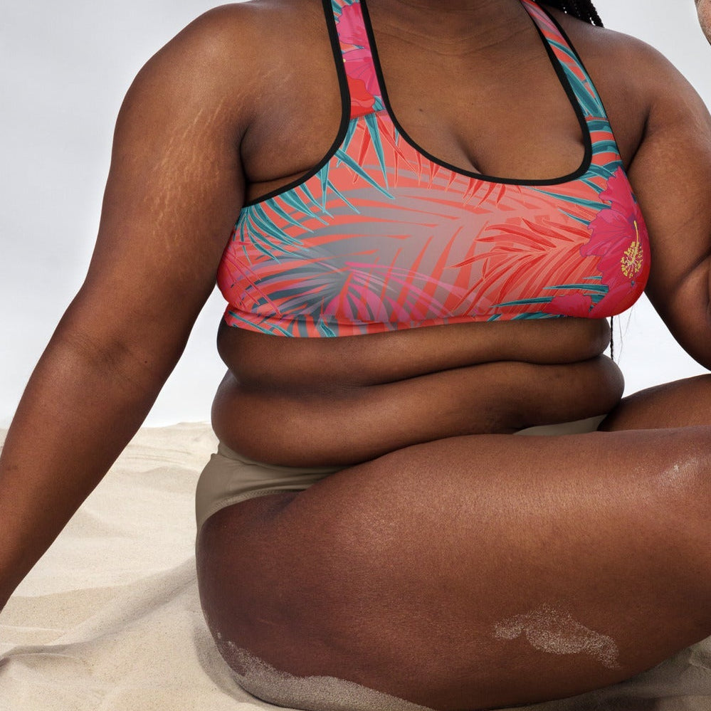 Close-up of a model wearing the District Tropics Performance Bra. The image showcases the vibrant pink and blue floral pattern, the supportive racerback design, and the premium mesh lining details.