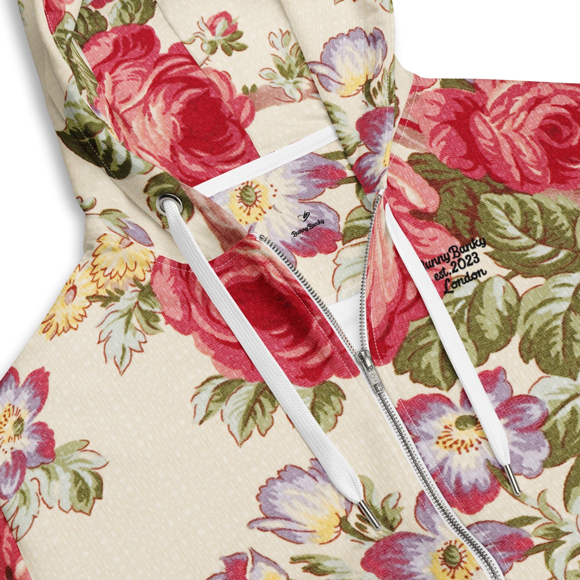 A close up of  the Evergreen Zip Hoodie, showcasing the elaborate red rose and green vine vintage print on a sustainable cream fabric.