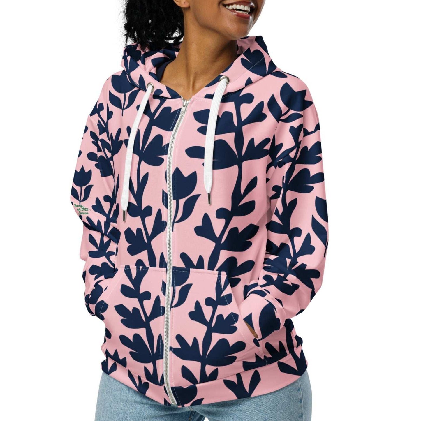 A model wearing The Kensington Zip Hoodie, showing the full-zip closure and the oversized pink and blue floral print across the recycled polyester fabric.