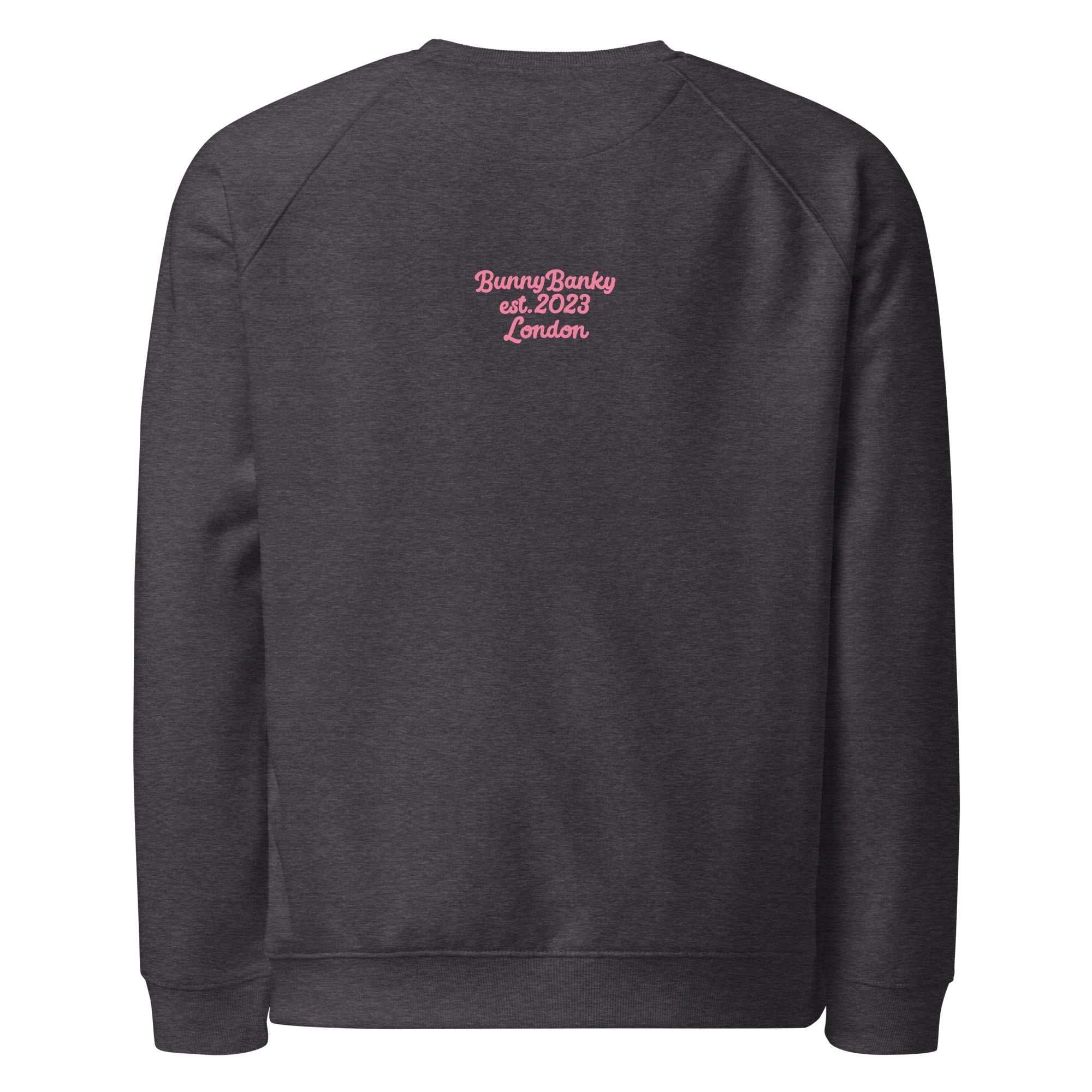A close-up of The Monument Organic Sweatshirt, showing the detailed embroidery of a vibrant pink heart with wings on the 100% organic cotton fabric.