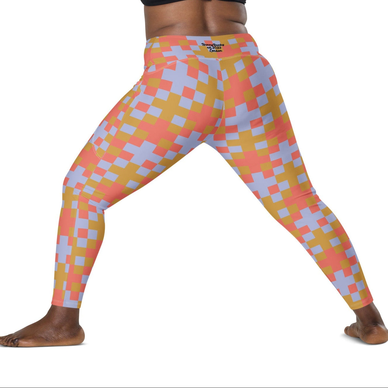 A model wearing the high-waisted Pixel Glam Sculpt Leggings, highlighting the colorful terracotta, gold, and blue pixelated grid pattern and the integrated side pocket design.