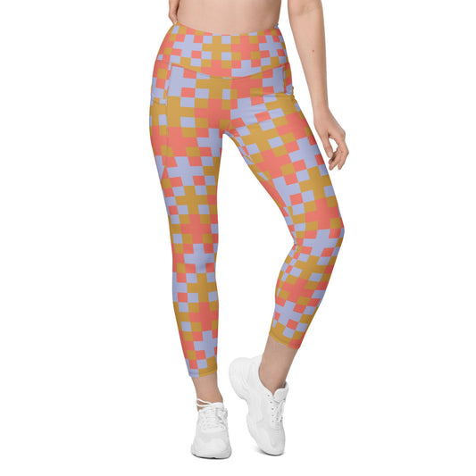 A model wearing the high-waisted Pixel Glam Sculpt Leggings, highlighting the colorful terracotta, gold, and blue pixelated grid pattern and the integrated side pocket design.