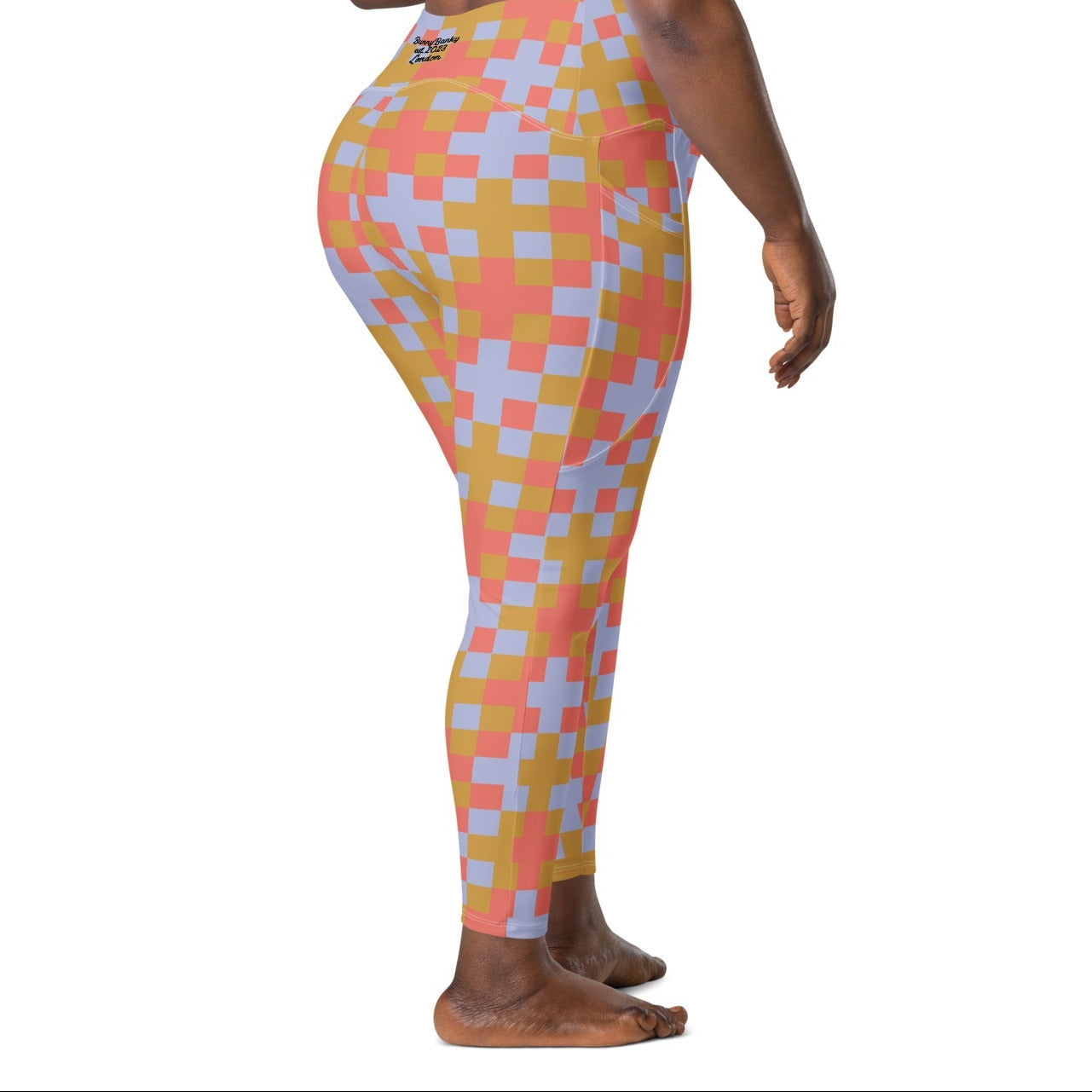 A model wearing the high-waisted Pixel Glam Sculpt Leggings, highlighting the colorful terracotta, gold, and blue pixelated grid pattern and the integrated side pocket design.