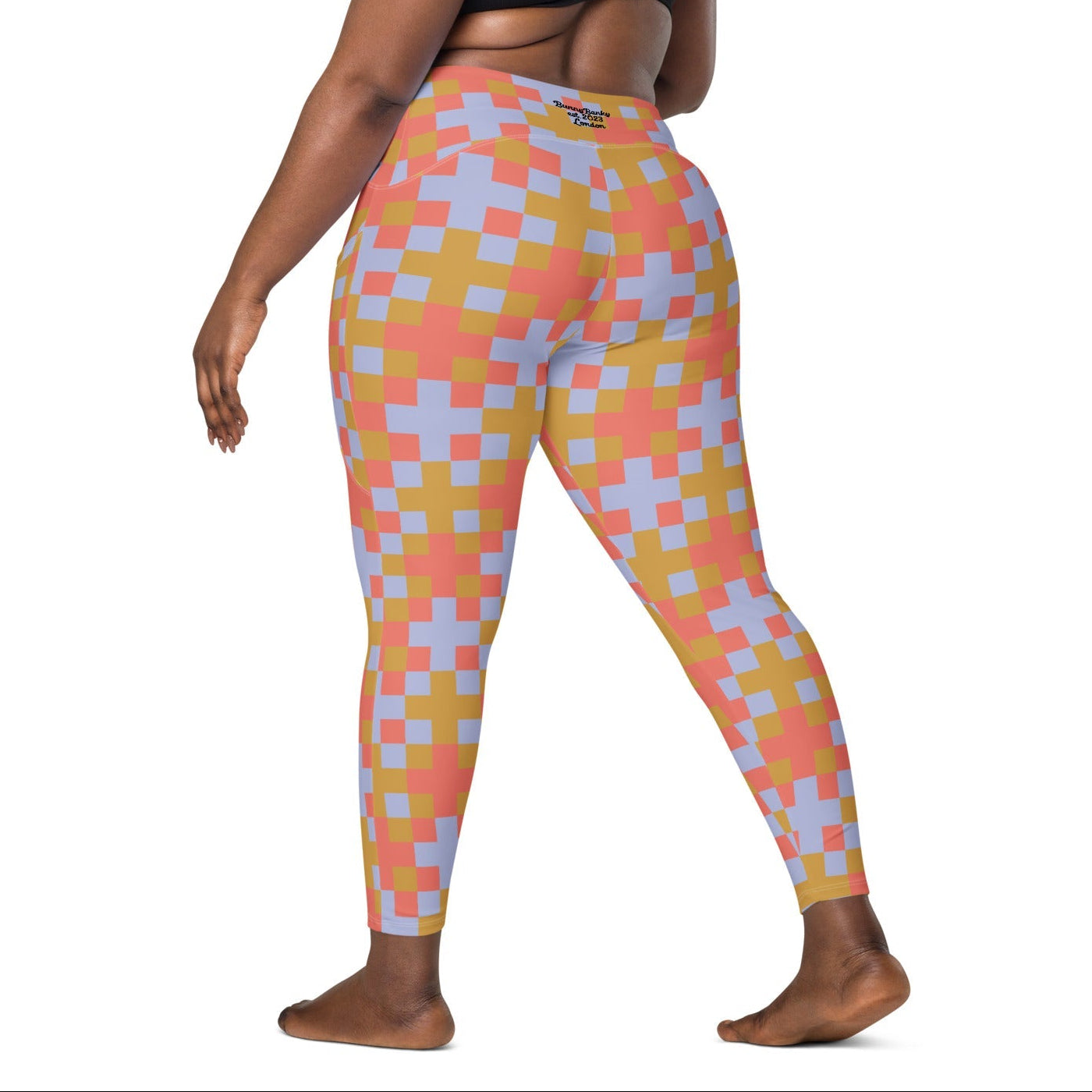 A model wearing the high-waisted Pixel Glam Sculpt Leggings, highlighting the colorful terracotta, gold, and blue pixelated grid pattern and the integrated side pocket design.