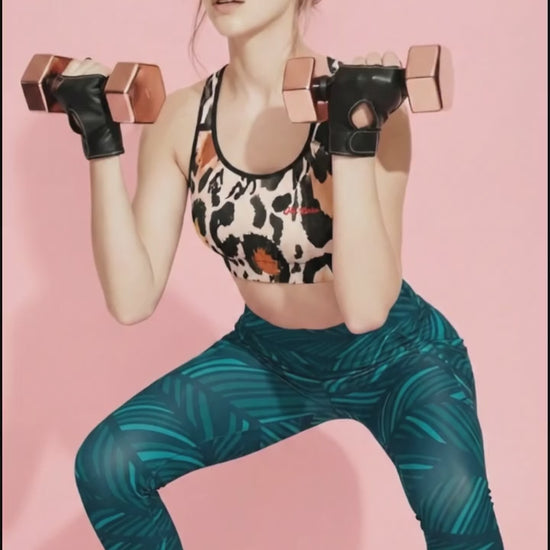 A high-quality product video featuring the Amazonia Performance Bra and Amazonia Sculpt Leggings. The model showcases the athletic fit and design within a fitness studio setting. The bra features a bold leopard animal print, while the leggings display a fluid, dark green curved leaf pattern. Subtle camera movements highlight the compression and flexible performance of the co-ord set against a soft pink background.