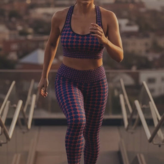 A BunnyBankY AI proprietary model wearing the complete Embankment set (Performance Bra and Sculpt Leggings) in a video. The model is actively going up stairs in a dynamic city open space, showcasing the sculpting fit and the high-contrast fuchsia and navy geometric print in motion.