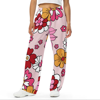 A model wearing the primrose hill flow joggers. pink wide-leg pants with a retro floral print, styled with a white crop top and white sneakers against a plain white background.