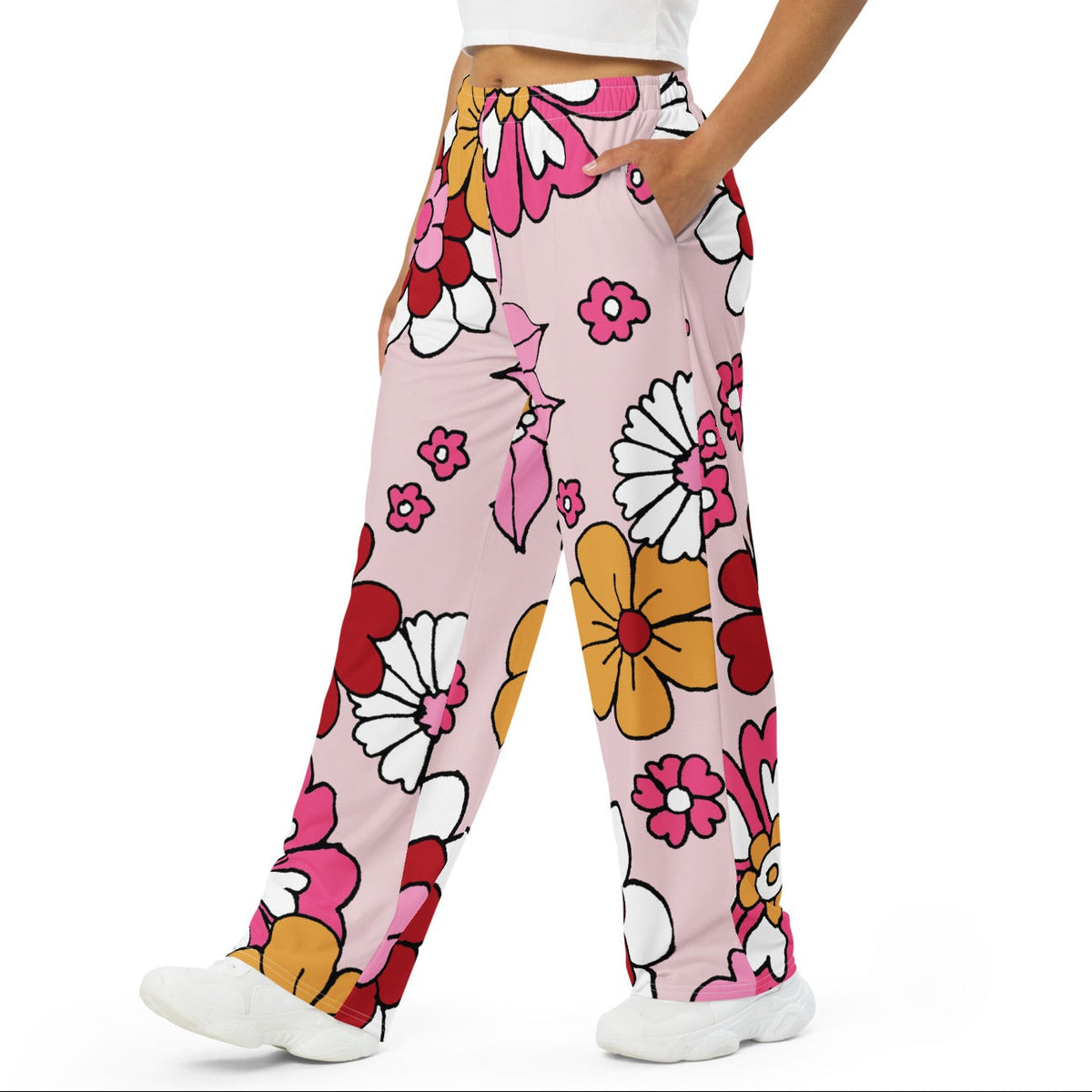 A model wearing the primrose hill flow joggers. pink wide-leg pants with a retro floral print, styled with a white crop top and white sneakers against a plain white background.