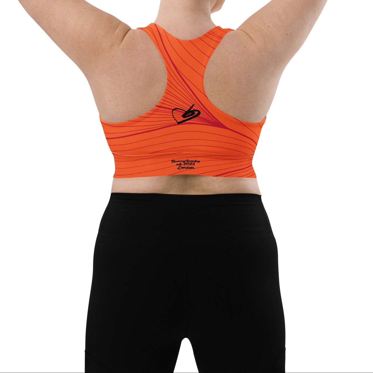 Model wearing the Rhodes Longline Performance Bra in vibrant orange geometric lines on orange background with the iconic logo and signature print at the back