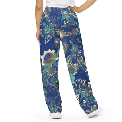 A woman is shown from the back wearing the rio flow joggers, wide-leg cut with a detailed botanical pattern in blue, green, and gold, paired with a white t-shirt and white sneakers, set against a plain white background.