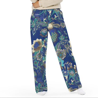 A woman wearing the rio flow joggers, wide-leg cut with a detailed botanical pattern in blue, green, and gold, paired with a white t-shirt and white sneakers, set against a plain white background.