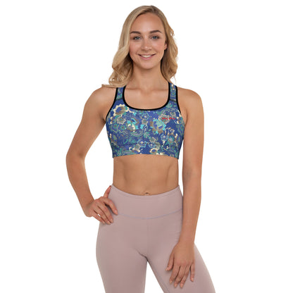 A model wearing The Rio Performance Bra, showing the supportive fit and the vibrant bright blue floral print with City Babe on the top left. Highlights the garment's construction from 74% recycled polyester.