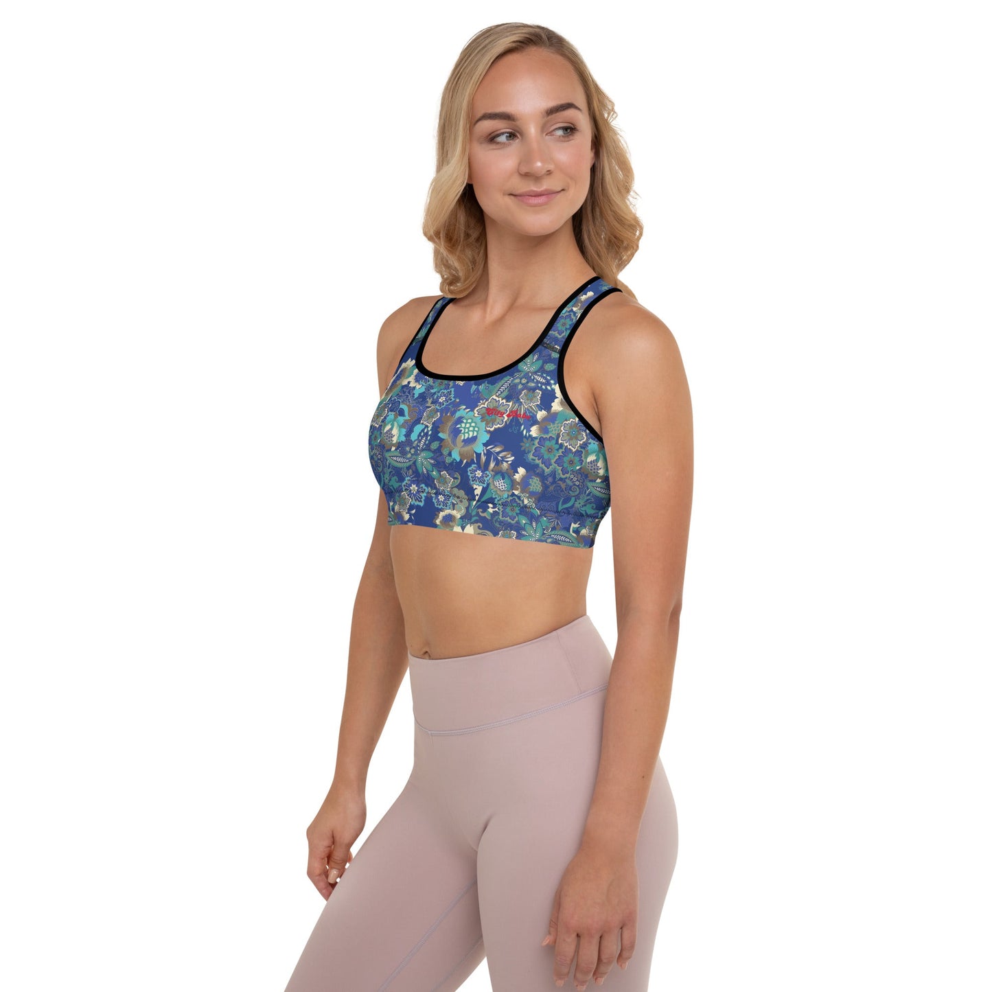 A model wearing The Rio Performance Bra, showing the supportive fit and the vibrant bright blue floral print. Highlights the garment's construction from 74% recycled polyester.