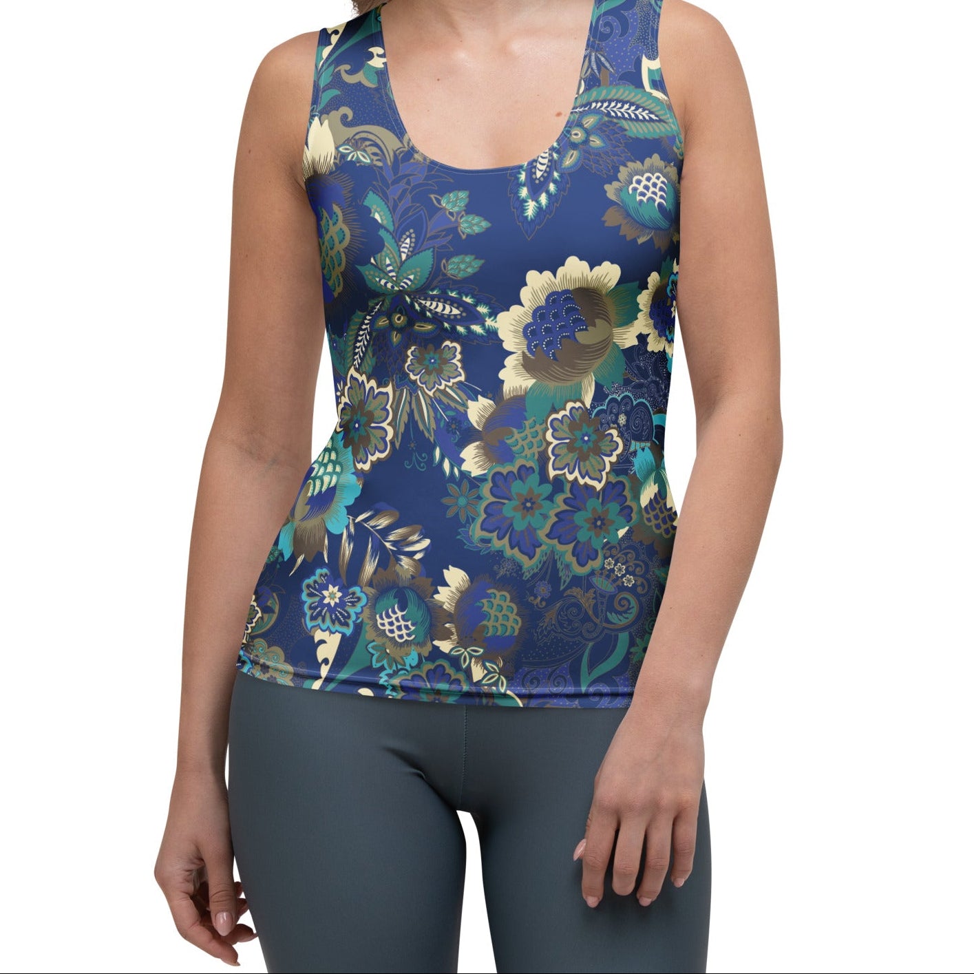 A woman modeling the rio performance tank. a sleeveless athletic tank top with a detailed botanical and floral pattern in navy blue, teal, and gold, paired with dark gray leggings, against a plain white background.